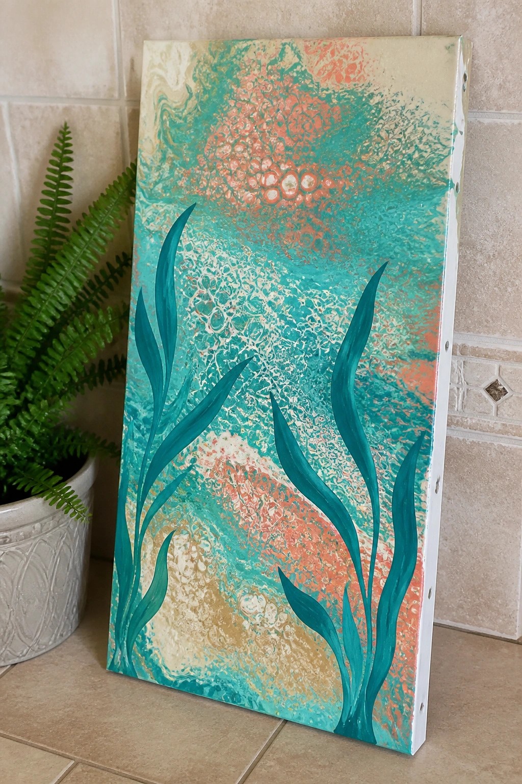 Abstract fluid painting with teal seaweed on marbled turquoise coral canvas beside fern plant