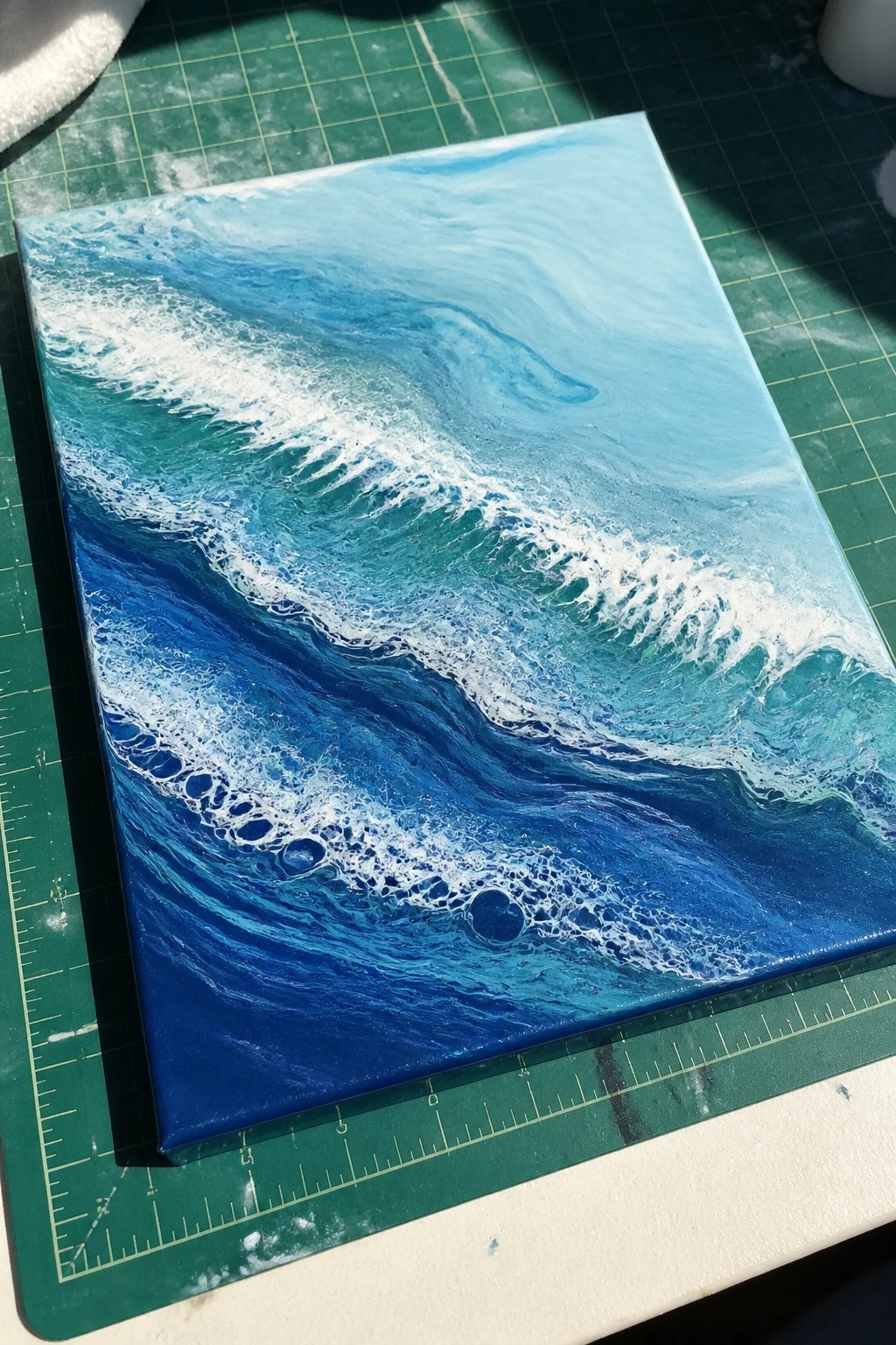 Ocean wave fluid painting in blues and white on canvas over green mat