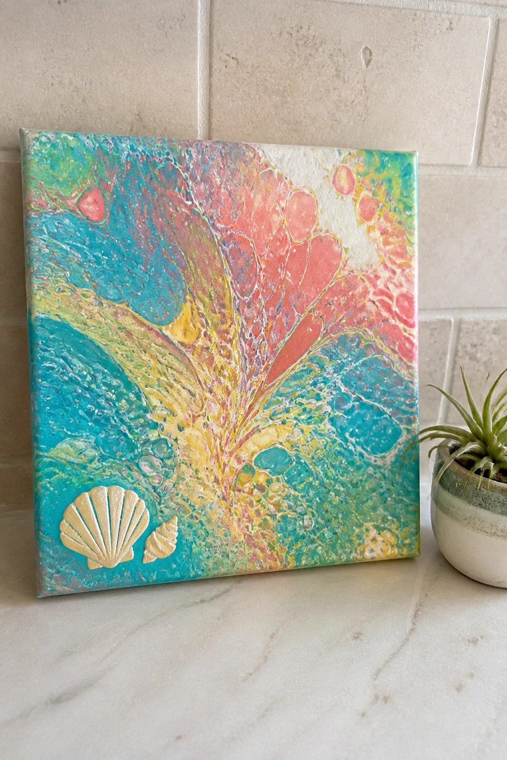Abstract fluid art canvas with pink teal yellow swirls and gold seashells on marble.