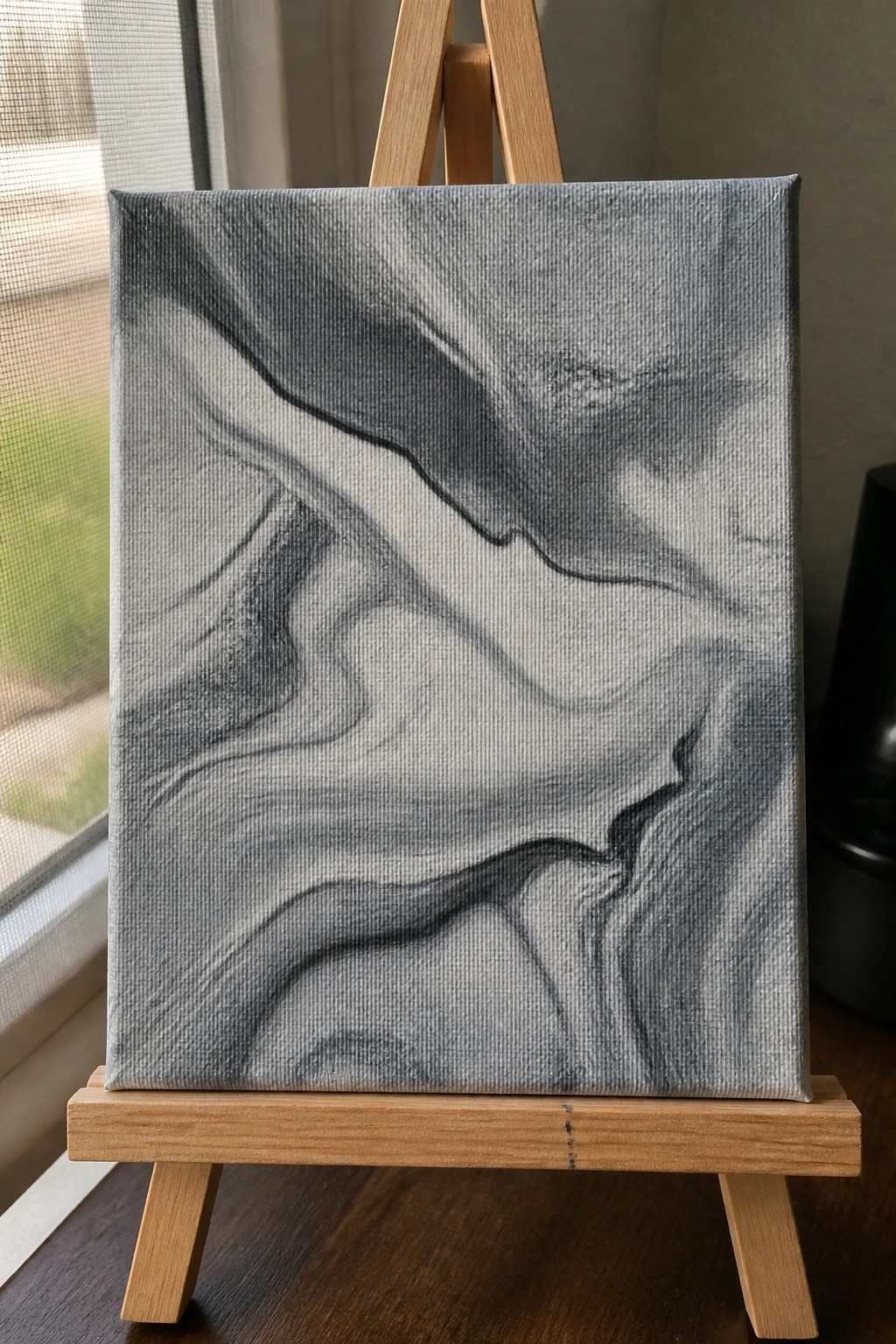 Abstract black and gray marbled painting on a small wooden easel.