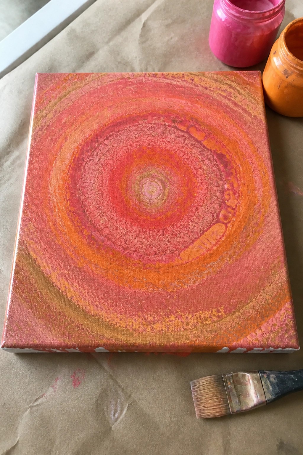Abstract canvas with swirling orange-pink circles, paint jars and brush on paper.