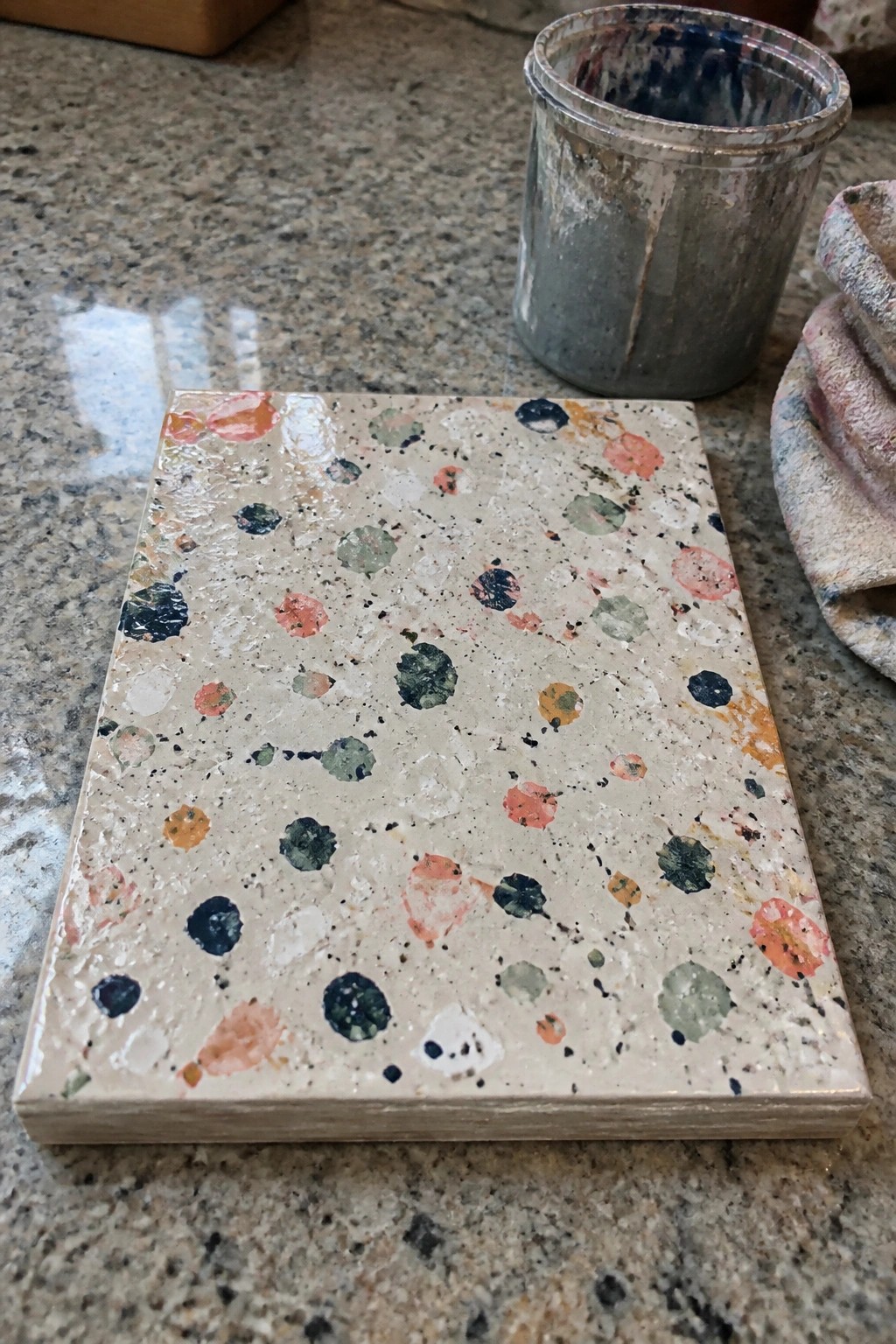 Colorful speckled tile sample on granite counter beside paint-splattered metal can