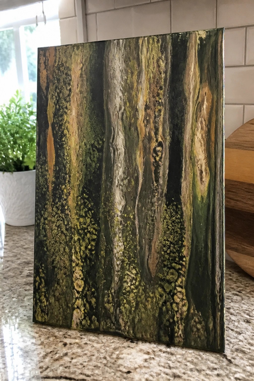Textured abstract panel with green, gold, and black vertical streaks on granite counter