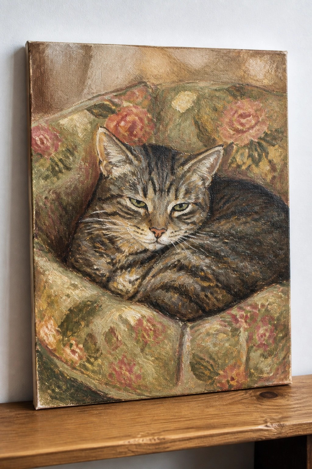 Tabby cat with green eyes curled on rose-patterned green floral cushion in oil painting