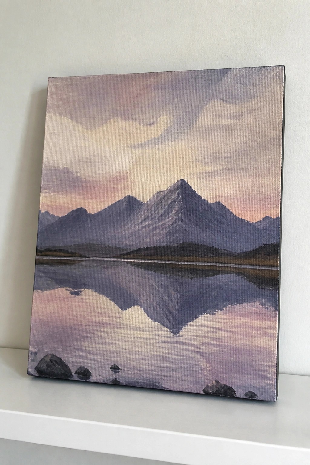 Painting of purple mountains reflected in calm lake under pink-orange sunset sky.