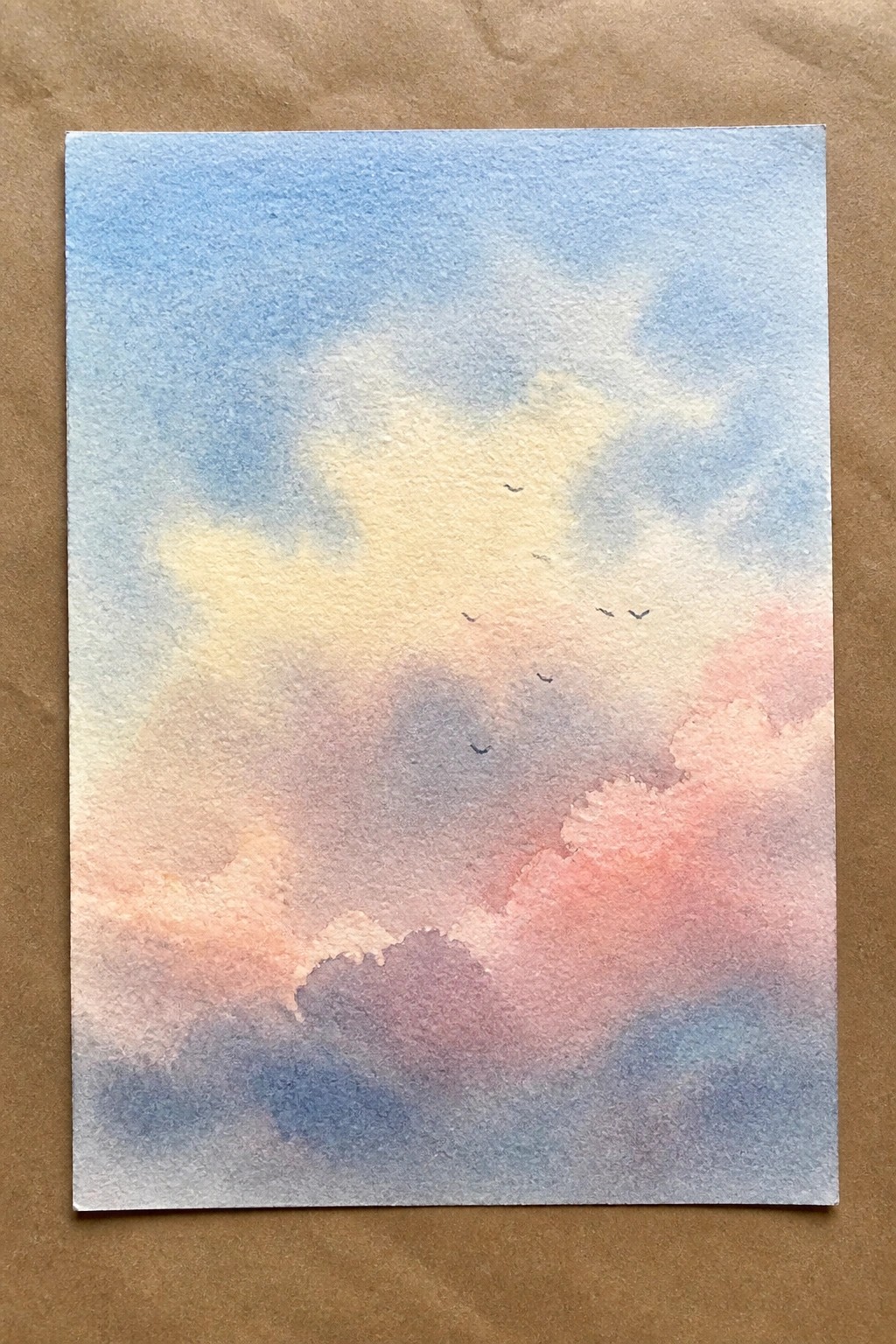 Watercolor sky with soft pink, blue, and yellow clouds and flying birds