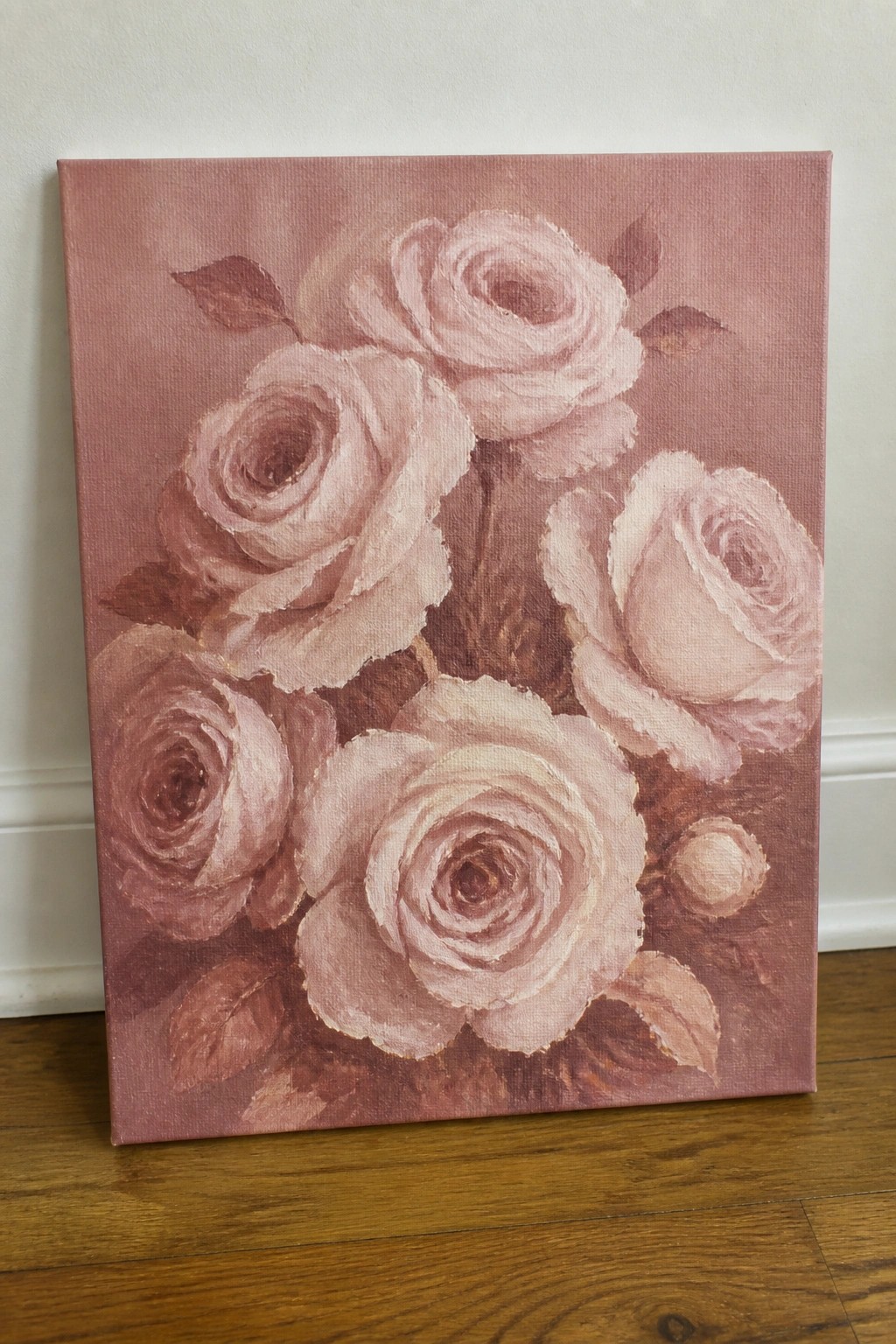 Painting of pink roses on canvas propped on wooden floor against wall