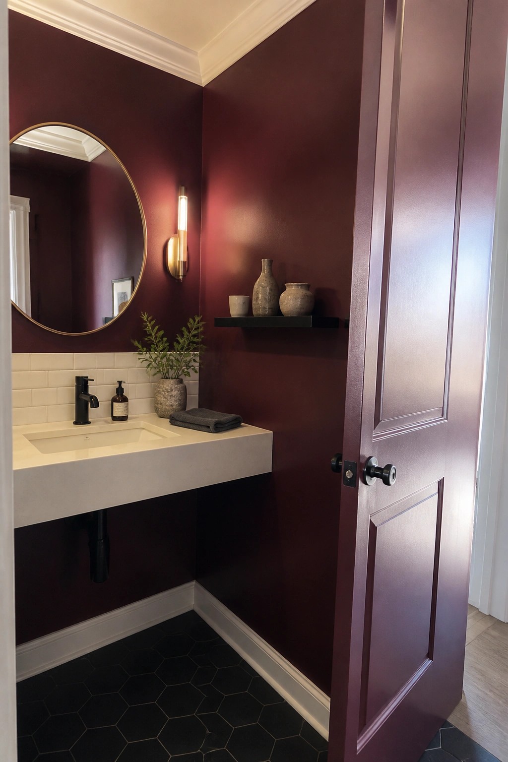 Deep burgundy walls in a small powder room with black hex tile floor and white floating sink.