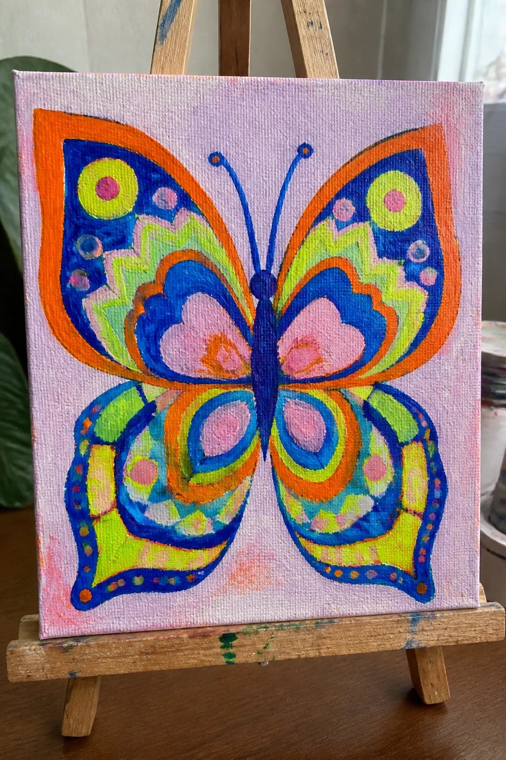 Colorful abstract butterfly painting on canvas atop a small wooden easel.