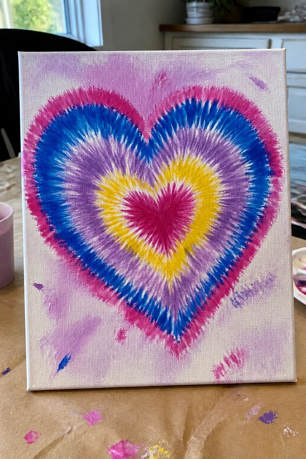 Tie-dye heart painting with pink, blue, purple, yellow rings on white canvas