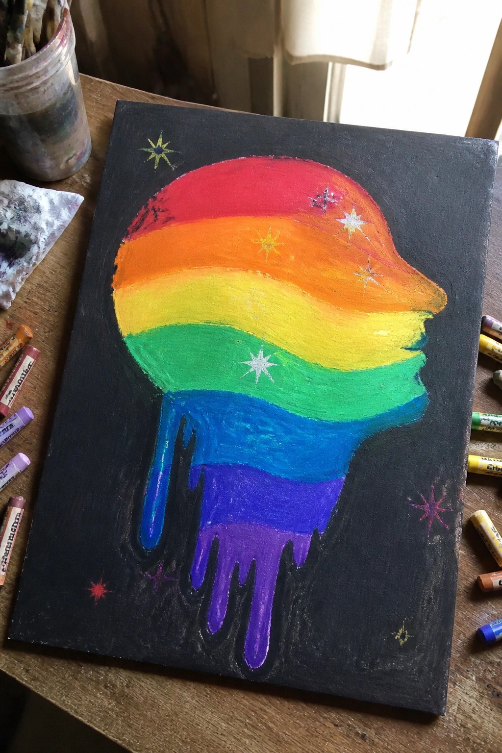Rainbow melting helmet painting with drips and stars on black canvas amid pastels
