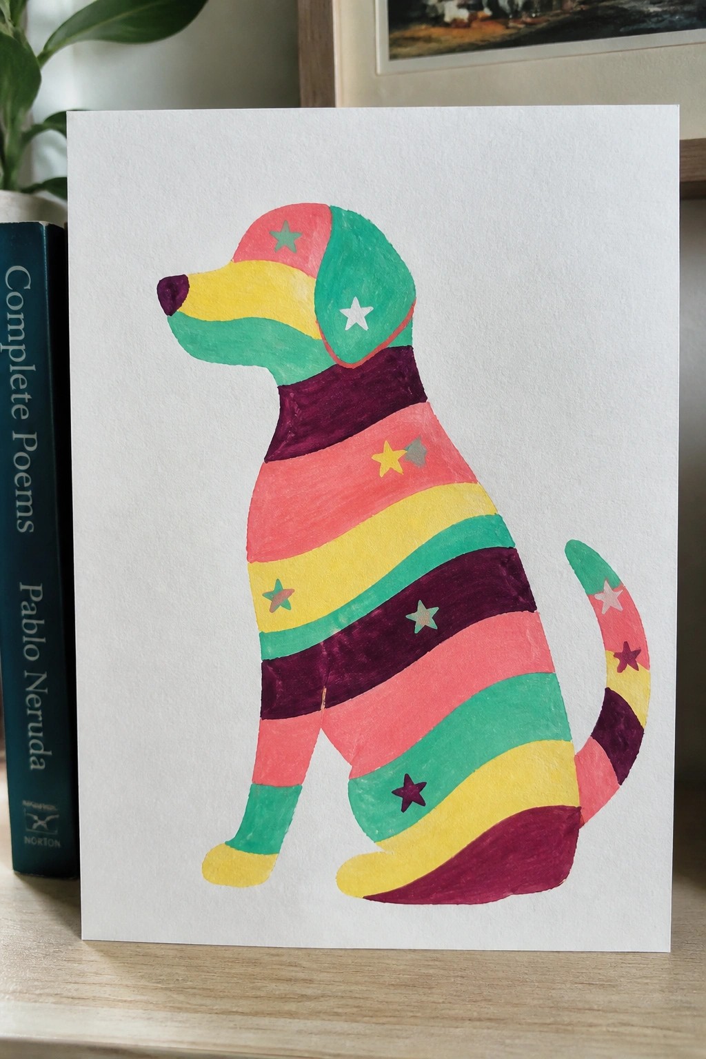 Colorful striped dog painting with stars beside Pablo Neruda poetry book.