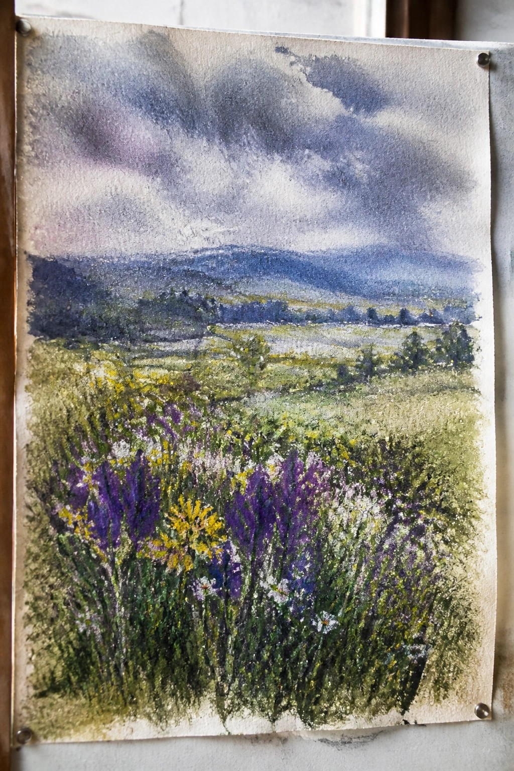 Watercolor painting of purple yellow wildflowers in meadow with cloudy hills beyond