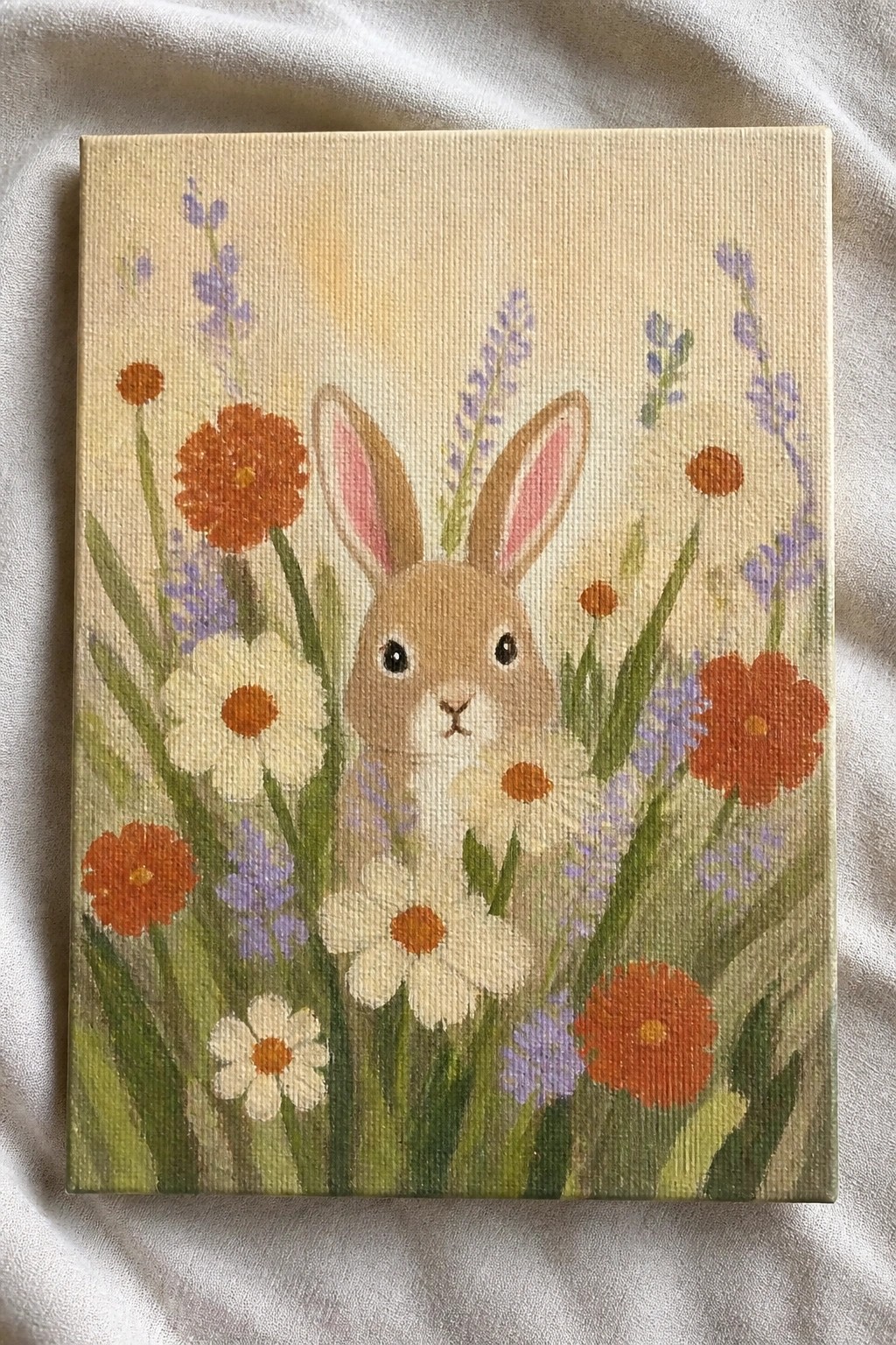 Brown rabbit with pink ears amid orange, white daisies and purple flowers on canvas
