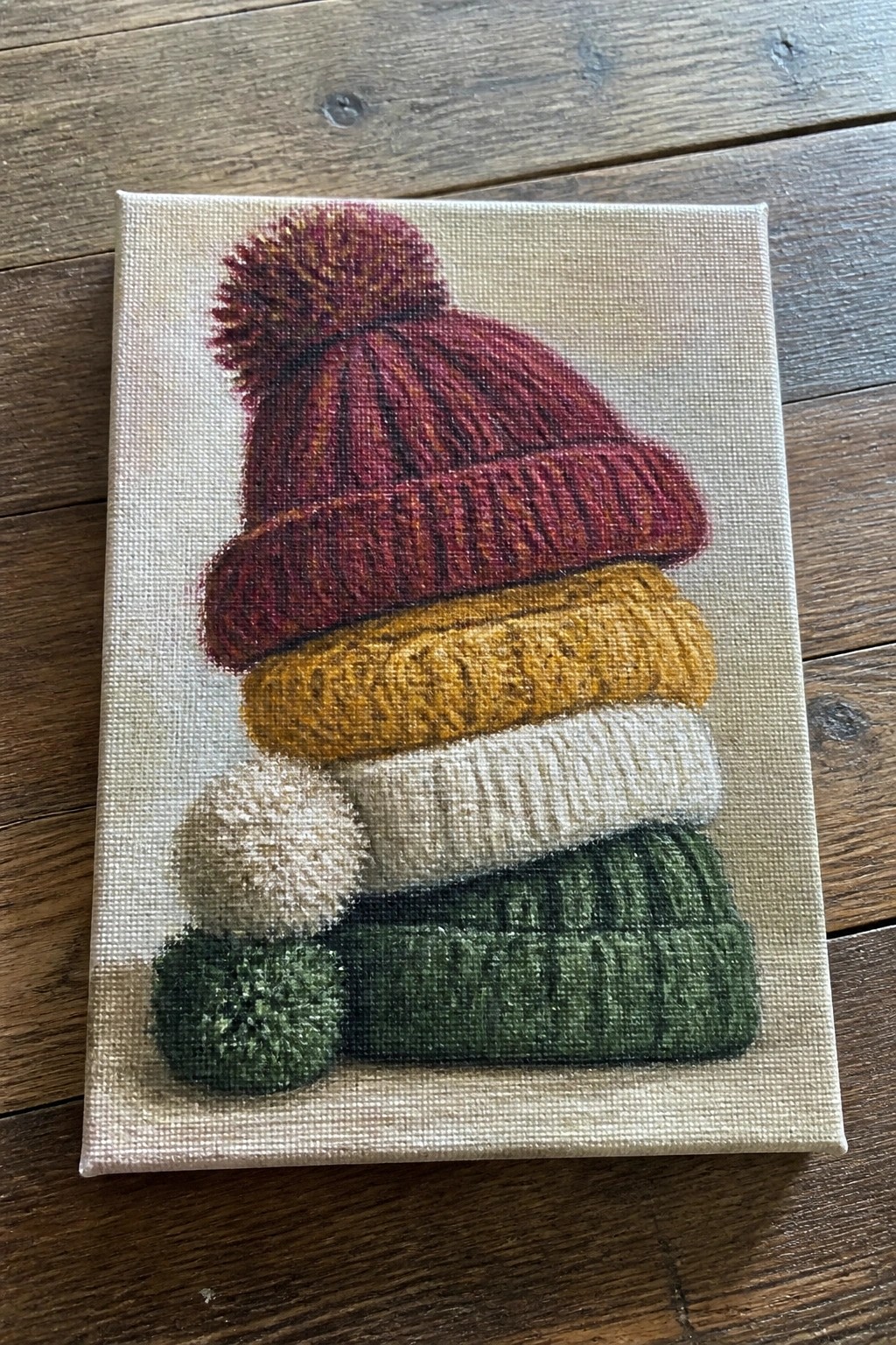 Stacked red, yellow, white, and green knitted winter hats with pom-poms on canvas