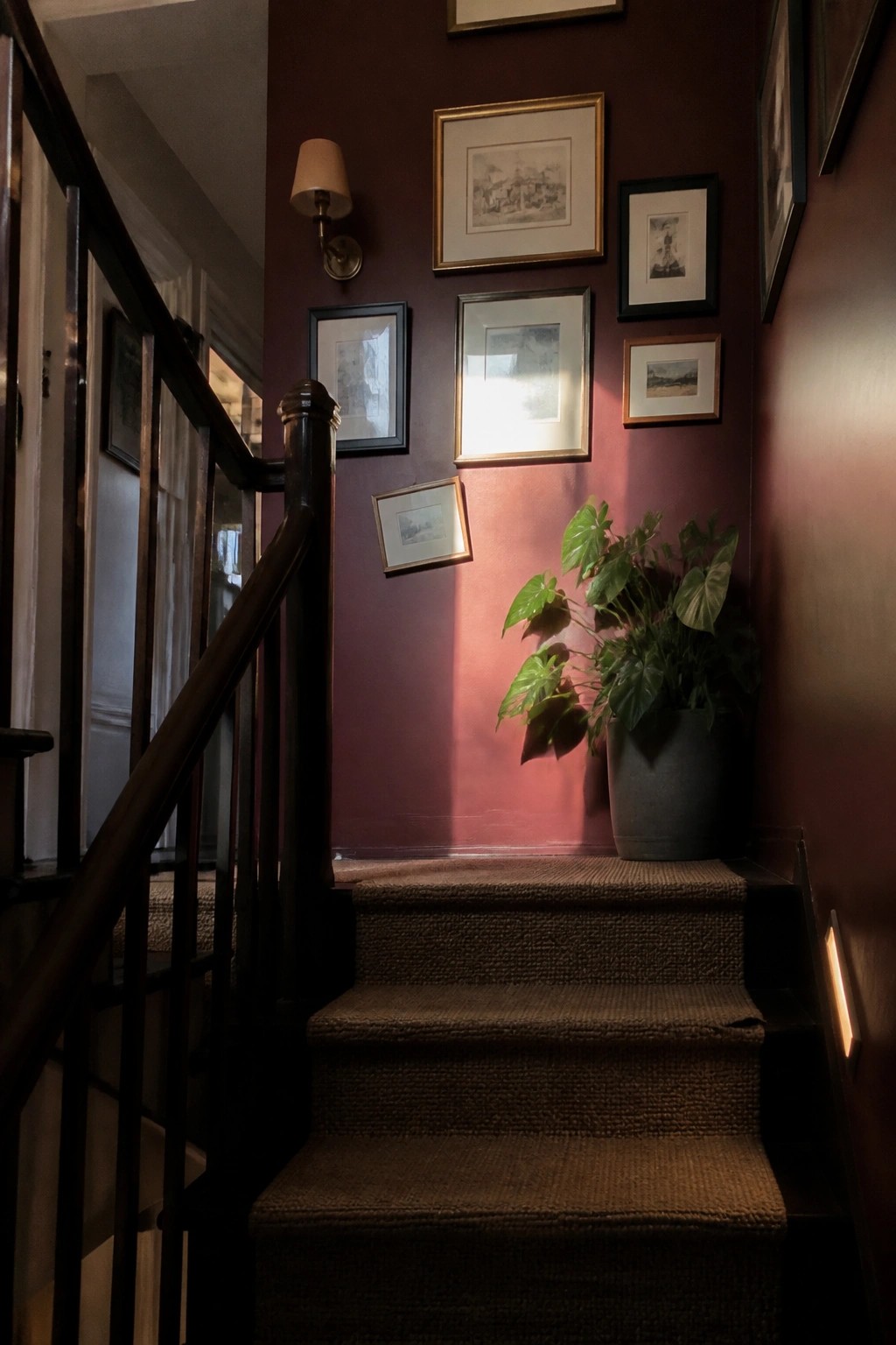 A deep red accent wall running along a narrow stairwell with dark wood railing.