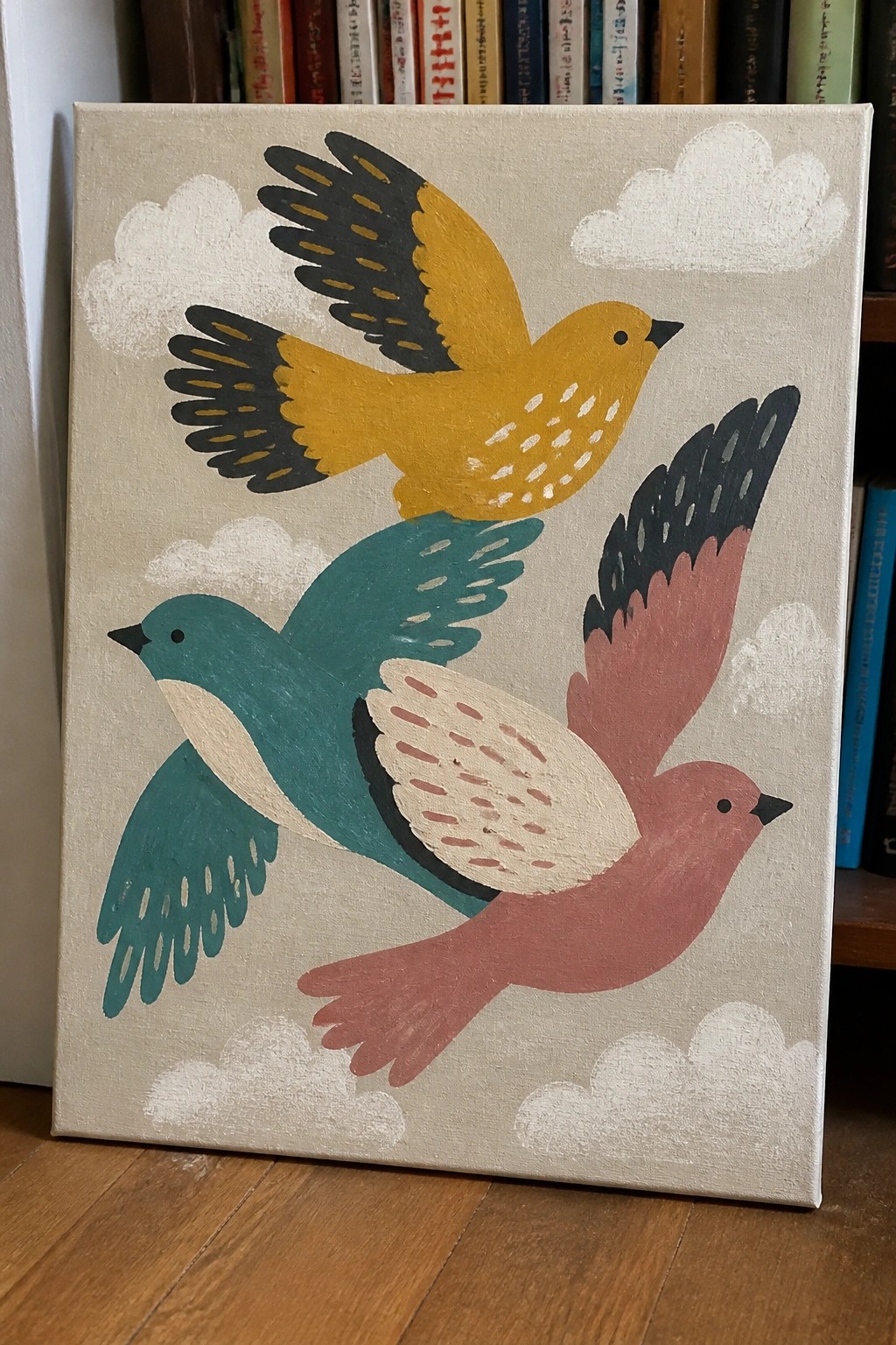 Canvas painting of three colorful birds flying amid white clouds on beige background