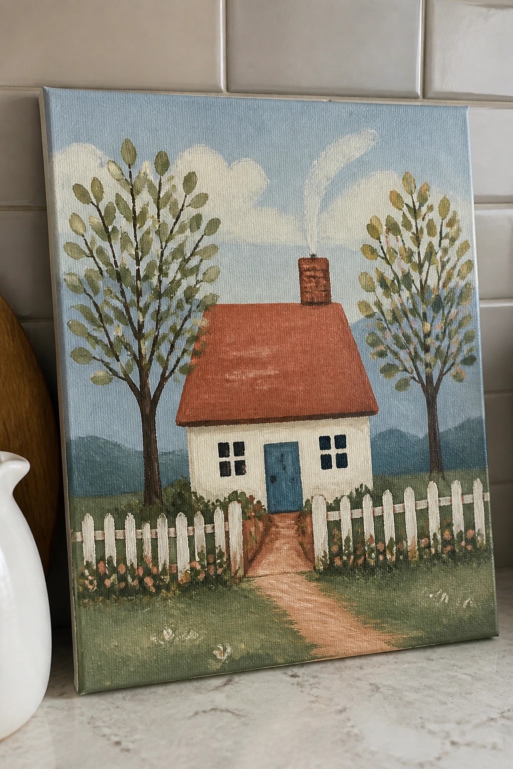 White cottage with red roof, blue door, white fence, trees, and dirt path.
