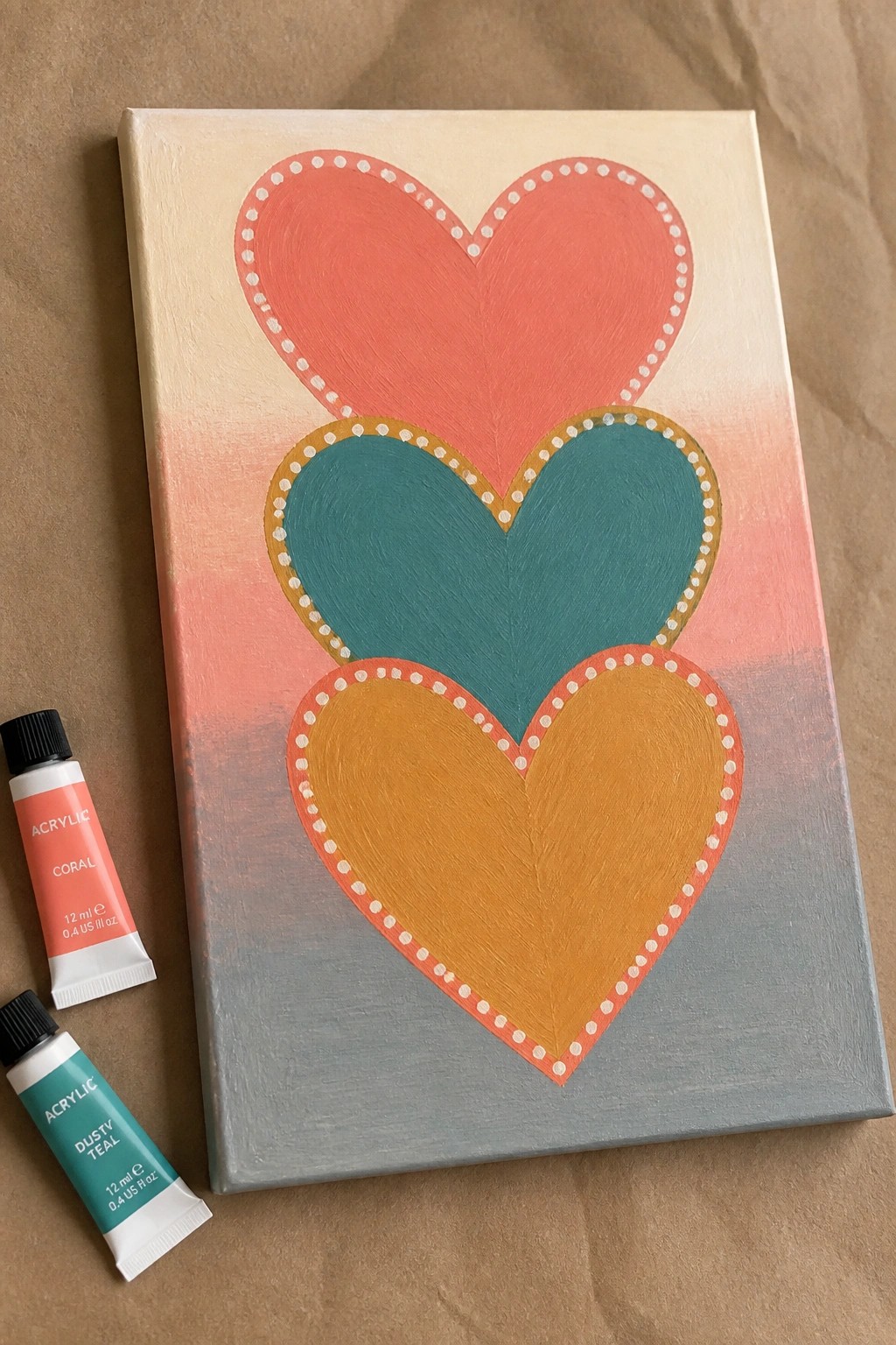 Canvas with coral, teal, and mustard hearts beside acrylic paint tubes.