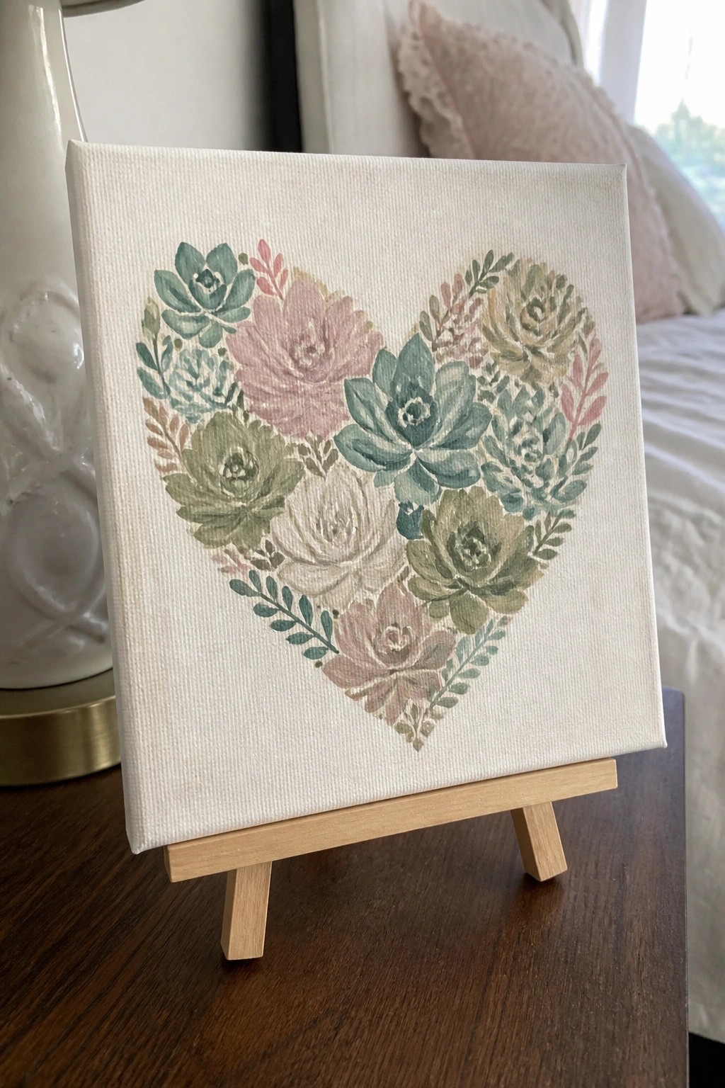 Pastel watercolor heart of succulents on white canvas atop wooden easel