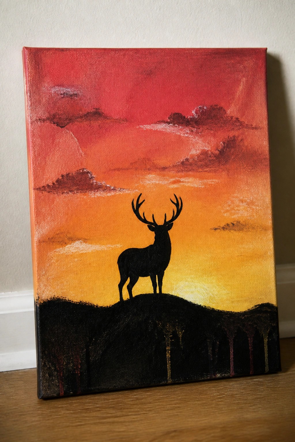 Silhouetted stag with antlers on black hill under red-orange sunset sky on canvas