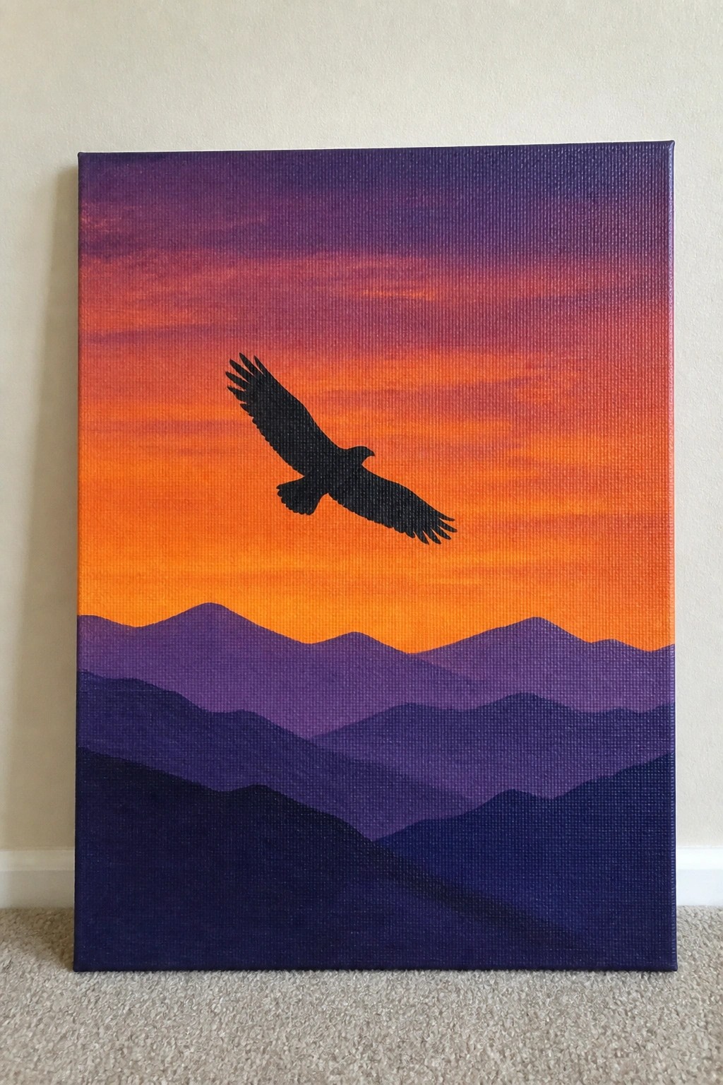 Black eagle silhouette soars over layered purple mountains under vibrant orange-purple sunset sky.