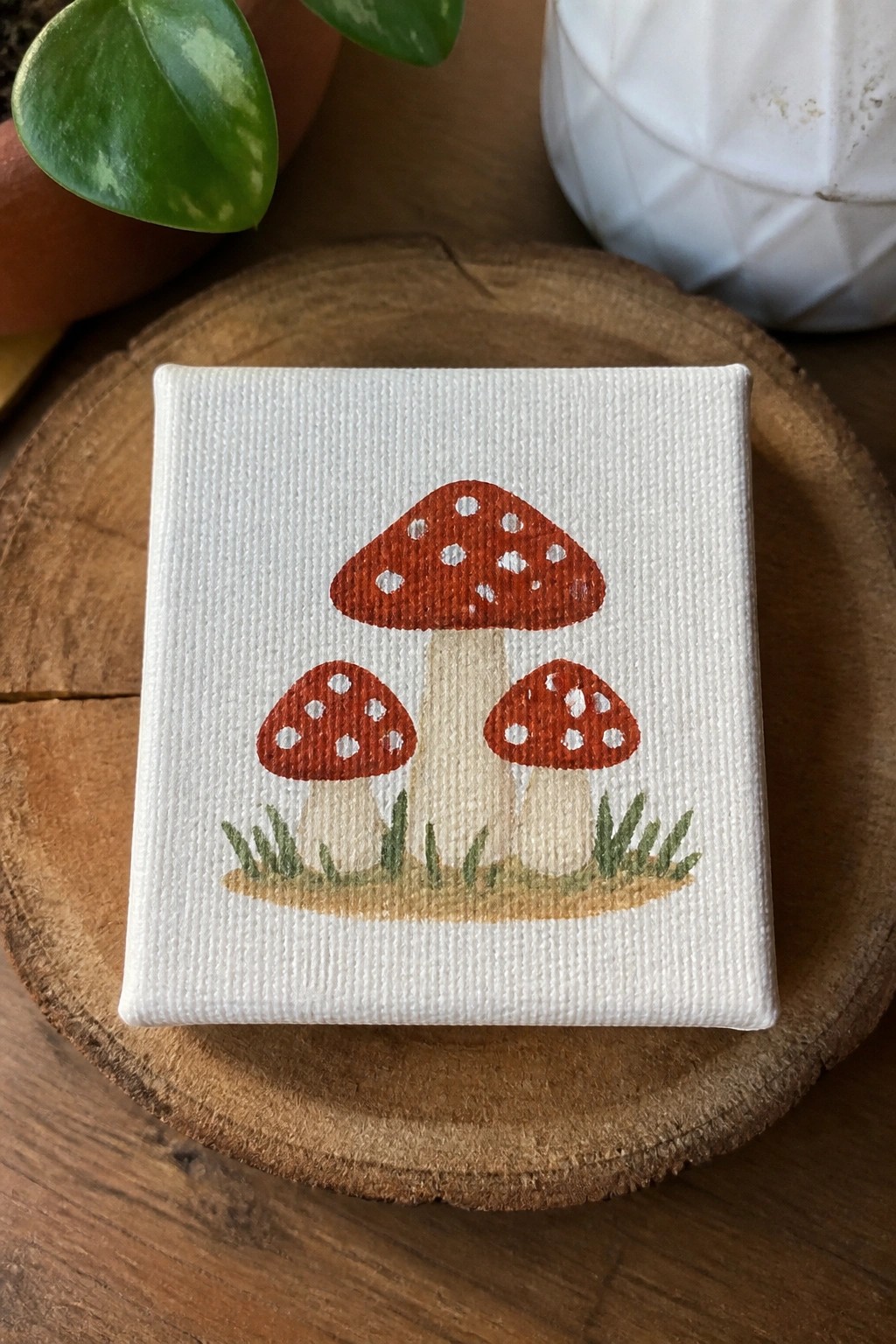 Small canvas painting of three red spotted mushrooms with grass on wood