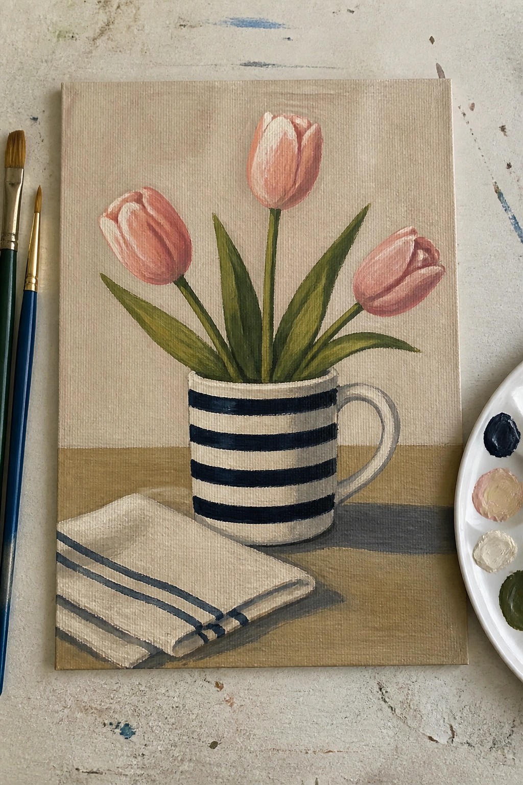Still life painting of three pink tulips in striped mug with napkin and brushes