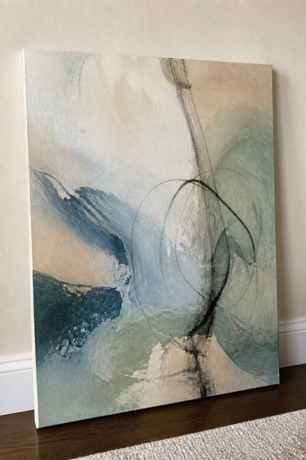 Abstract canvas painting with soft blue green and beige swirls leaning on wall