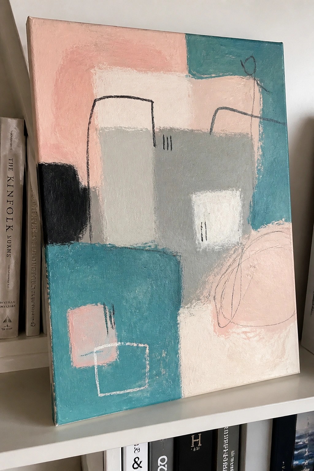 Abstract painting with pink, teal, gray shapes on white shelf among books