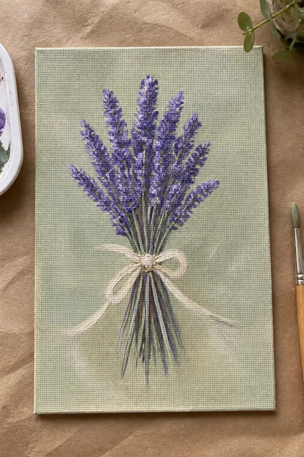 Lavender bouquet painting with cream bow on light green canvas amid art supplies
