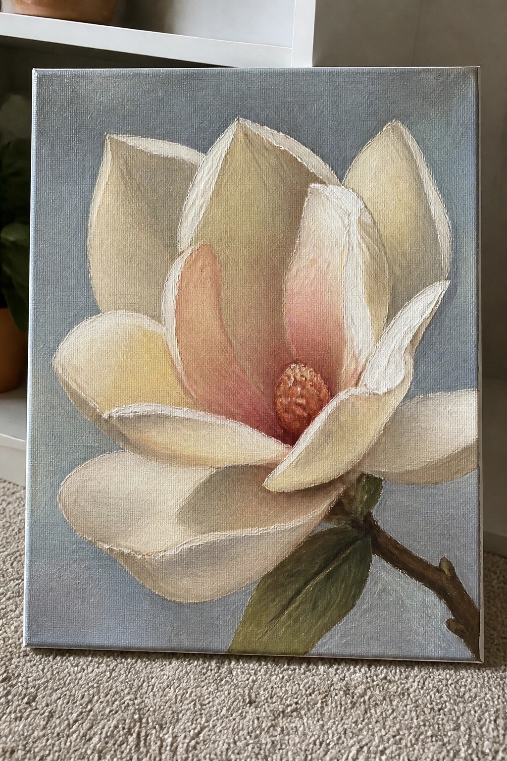 Painting of white magnolia with pink center and green leaves on gray canvas