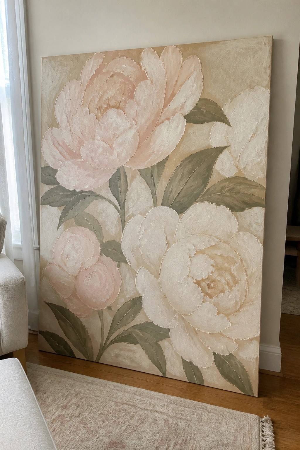 Large painting of pink and white peonies leaning against a wall on wooden floor