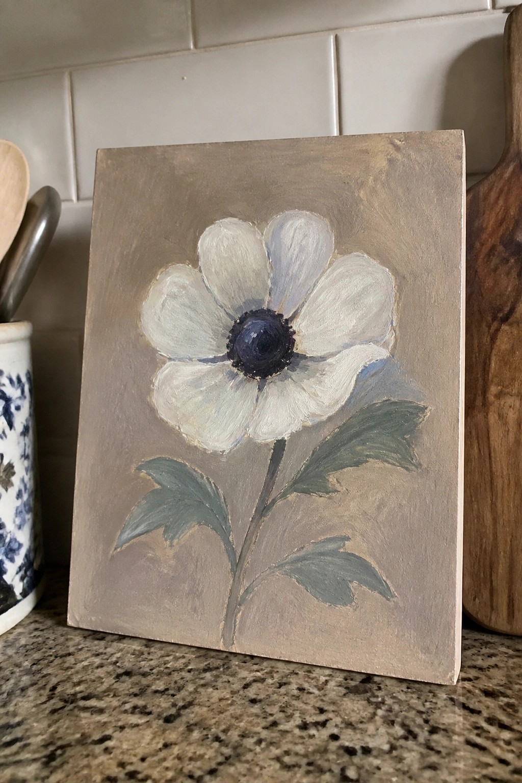 White flower with dark blue center and green leaves painted on taupe canvas