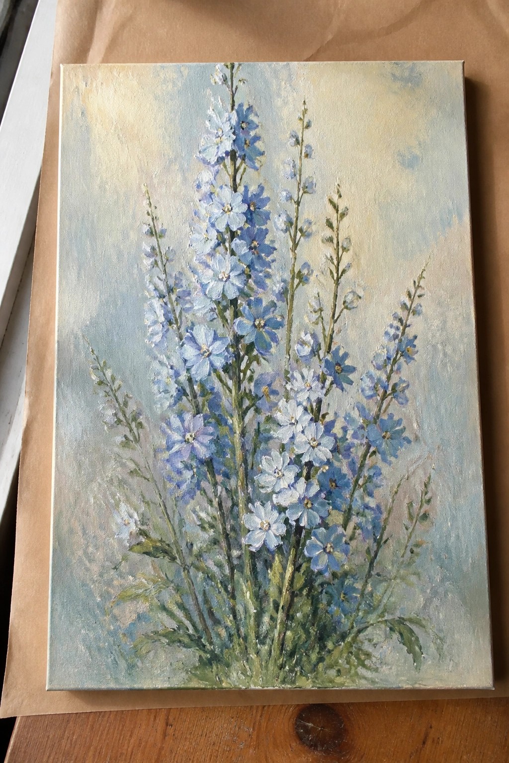 Oil painting of tall blue delphiniums with green stems and leaves on canvas