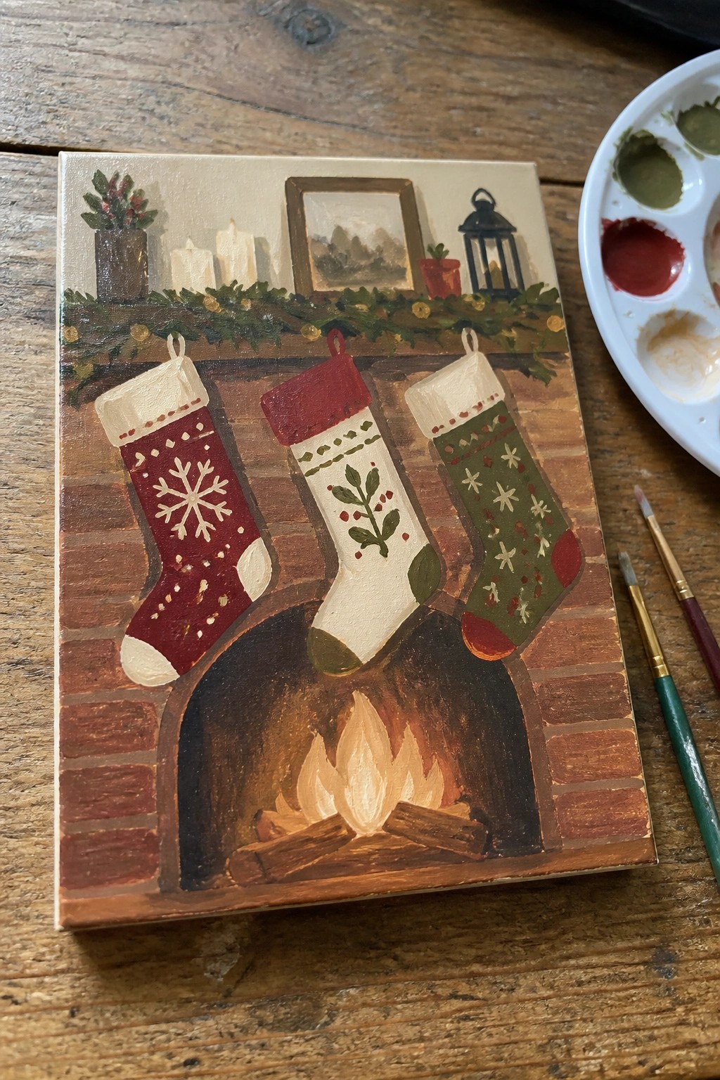 Three patterned Christmas stockings hang over a brick fireplace with glowing flames.