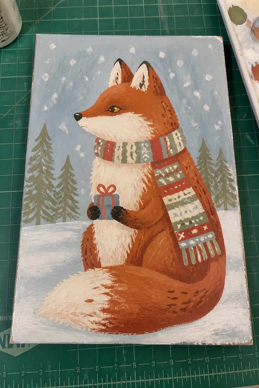 Fox wearing patterned scarf holds gift in snowy pine forest scene
