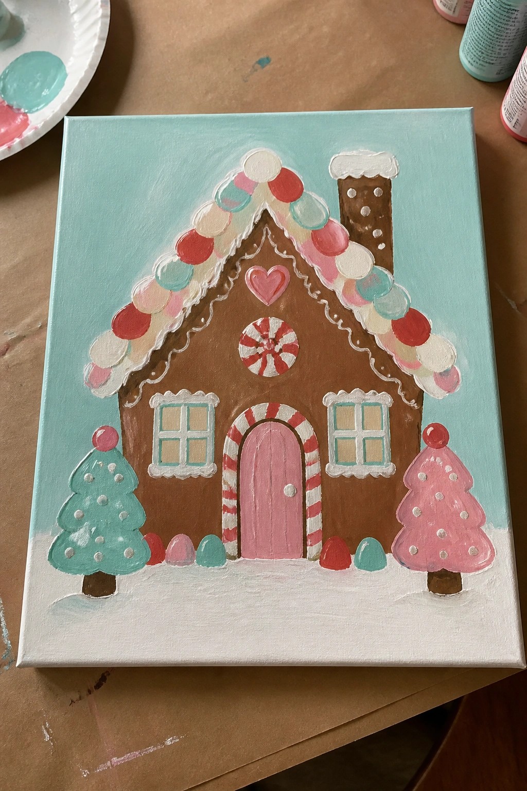 Colorful gingerbread house painting with candy roof, pink door, and pink teal trees on snow