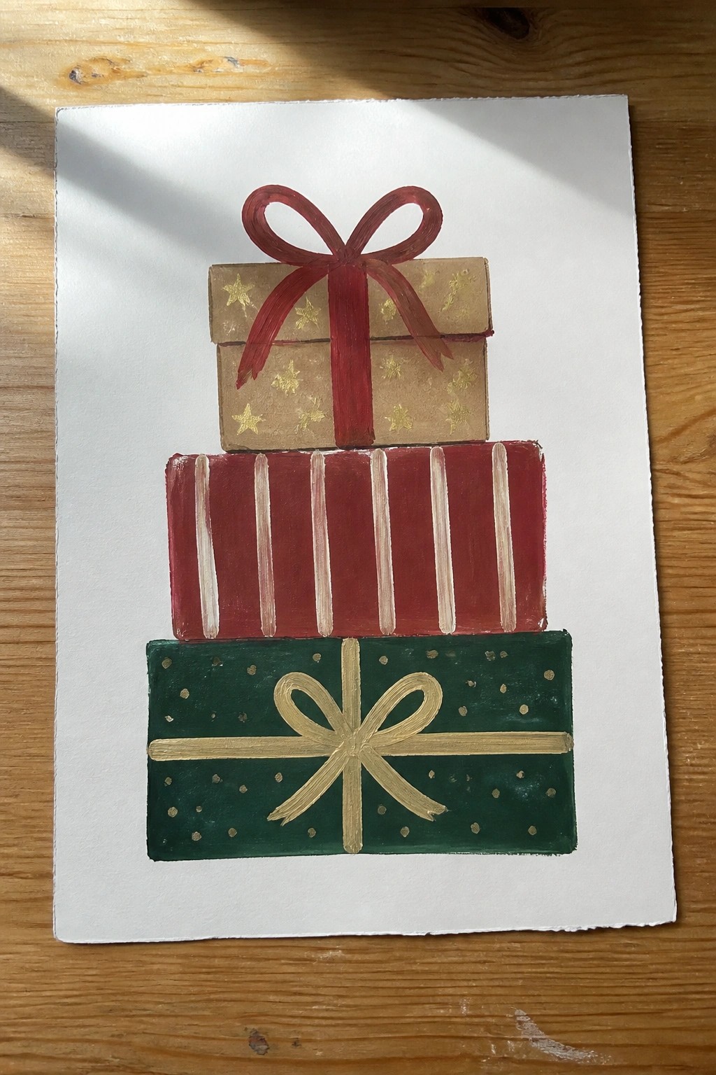 Acrylic painting of three stacked Christmas gift boxes with red, brown, and green wrapping plus ribbons on white paper.