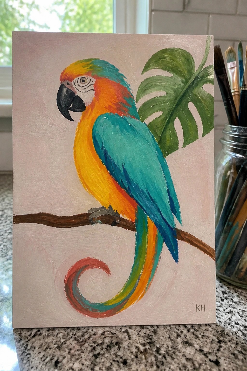 Vibrant macaw painting in yellow orange teal on branch with green leaf and brushes nearby