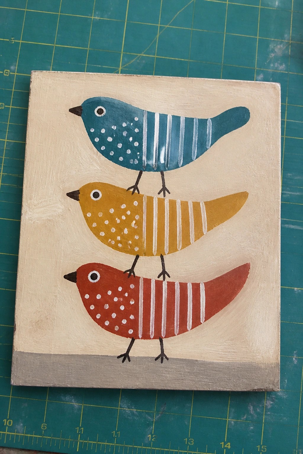 Three stacked folk-art birds in teal, yellow, and red on beige canvas