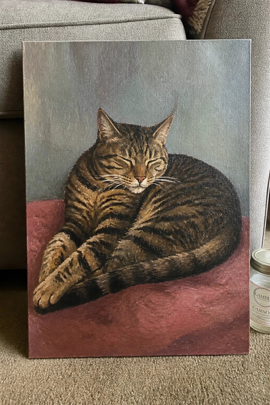 Sleeping tabby cat curled on red surface in realistic oil painting with gray backdrop