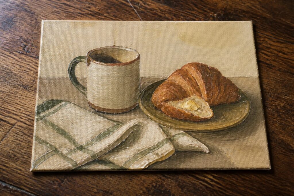 Still-life painting of buttered croissant on plate beside ceramic mug and striped napkin.