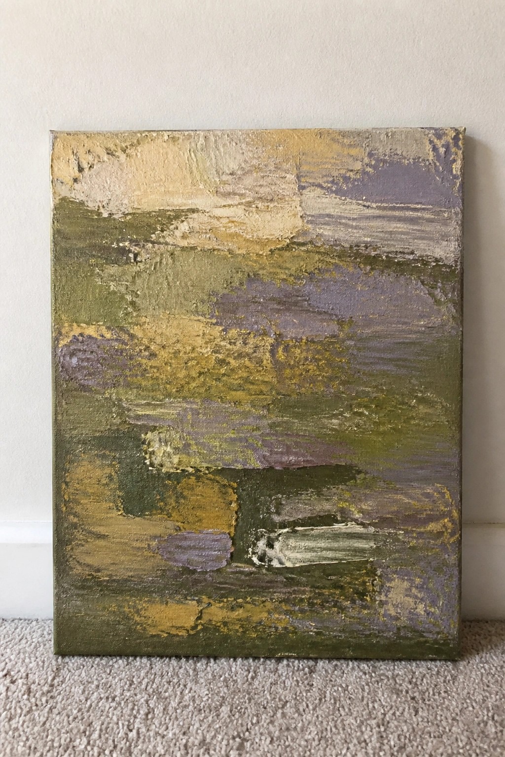 Abstract canvas with thick green, yellow, and purple brushstrokes against white wall on carpet.