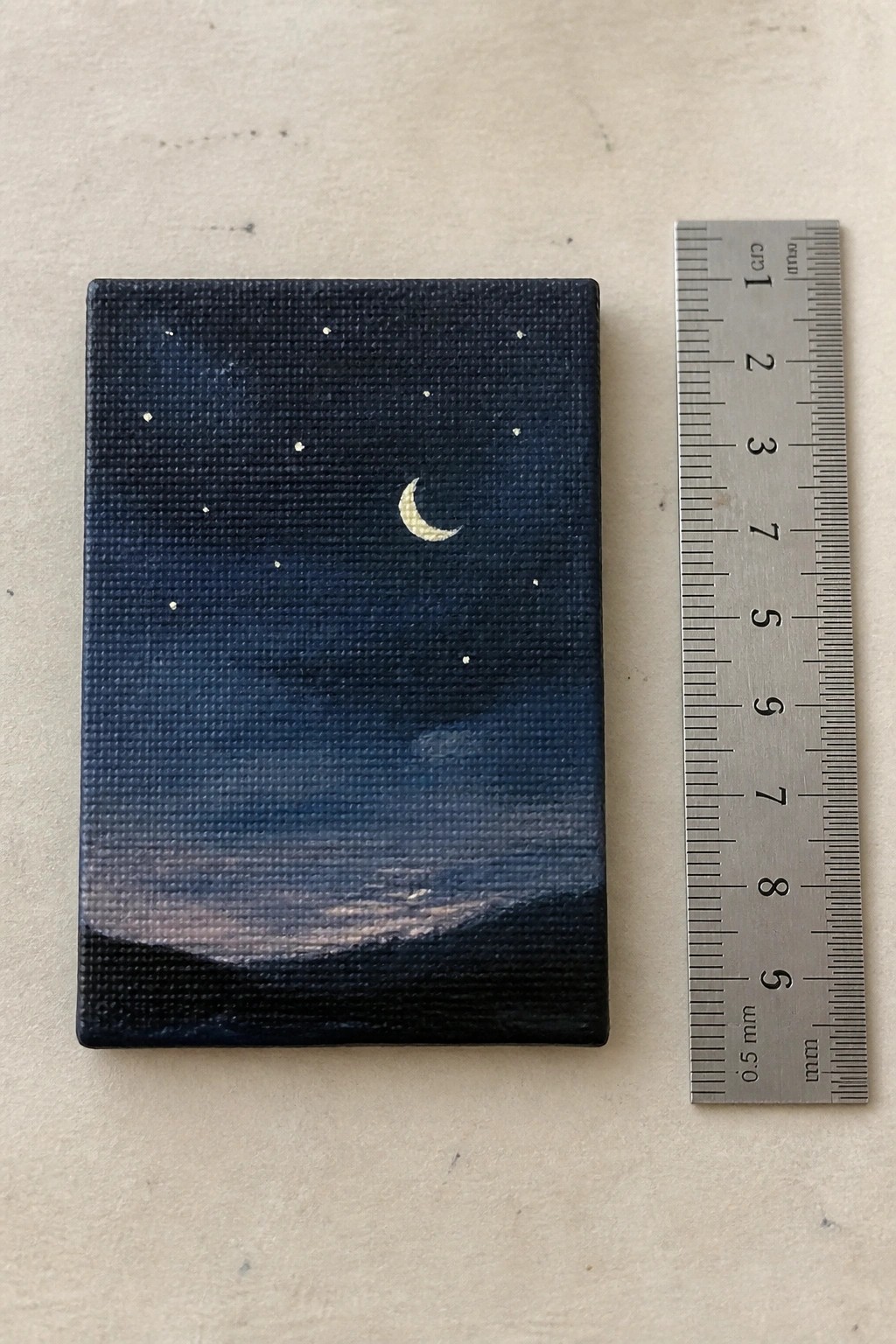 Small rectangular night sky painting with crescent moon and stars beside ruler