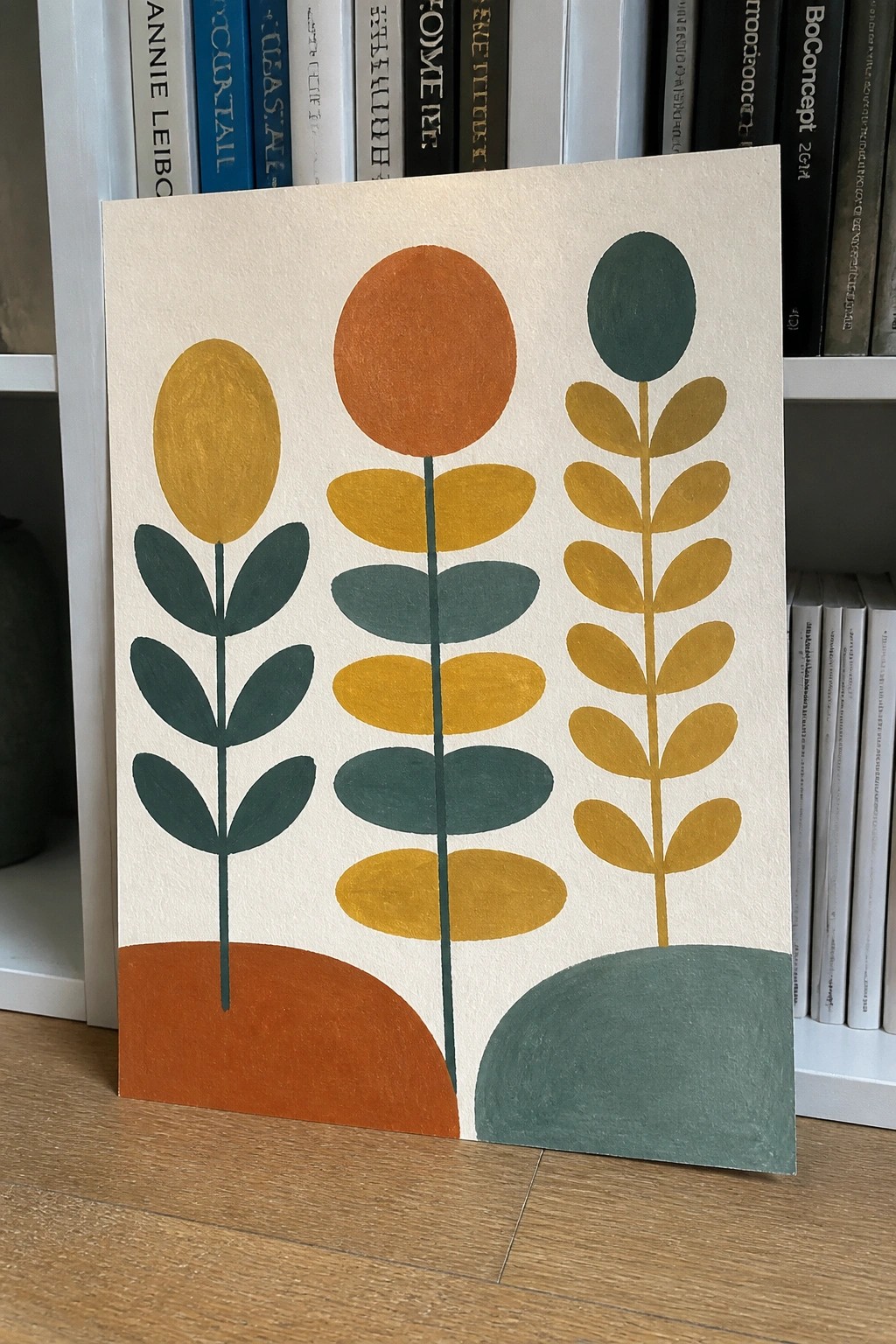 Abstract artwork of three stylized plants in yellow, orange, and teal before bookshelves.