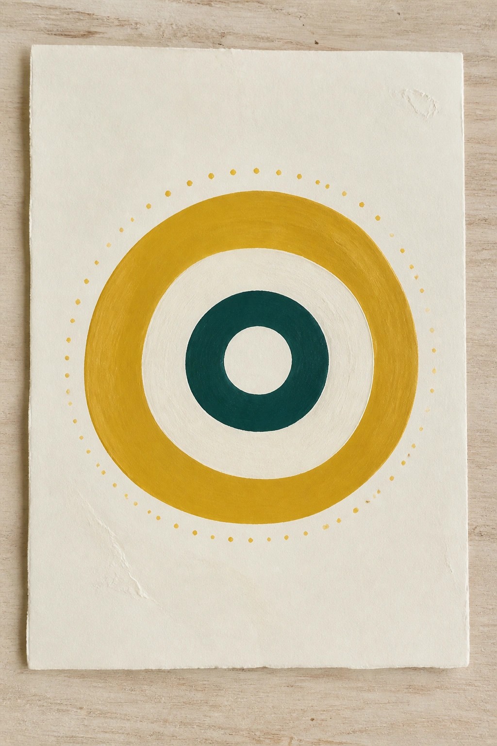 Concentric circles in mustard yellow, dark teal, and white on cream paper with dotted border