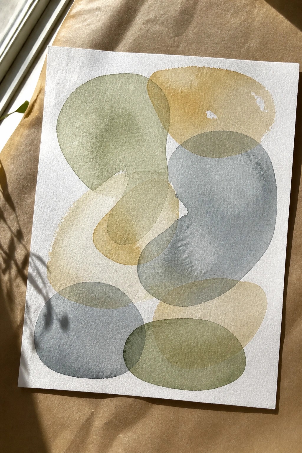 Abstract watercolor with overlapping translucent circles in soft green, blue, and beige tones on white paper