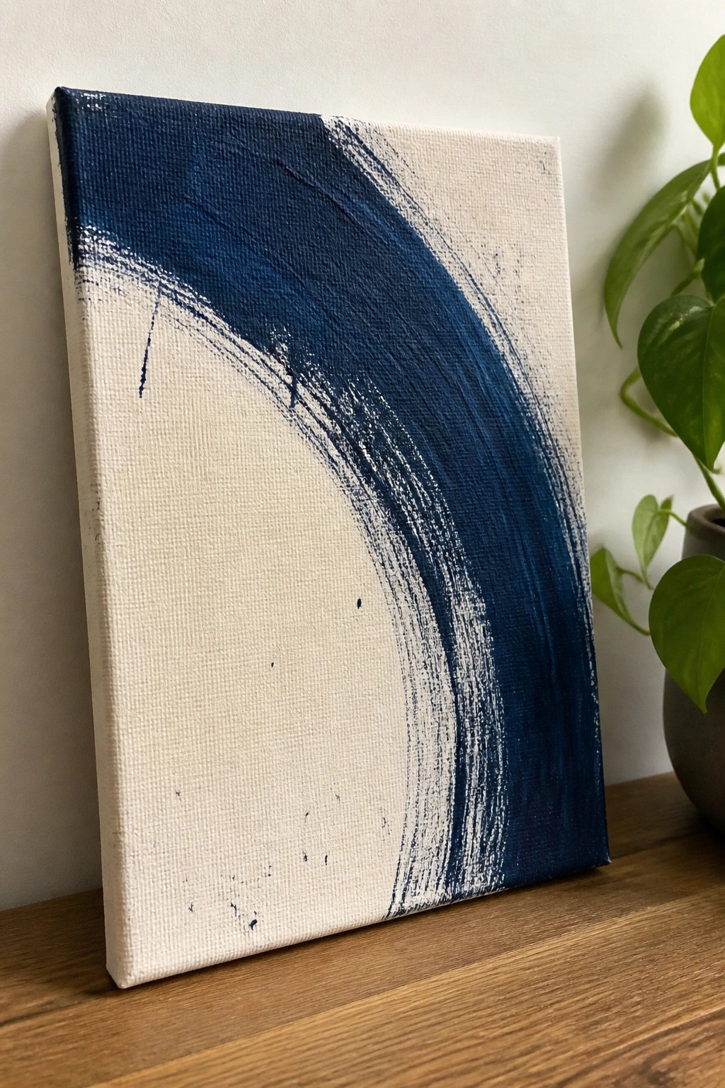 Abstract canvas with bold blue brushstrokes on white beside green plant on wood