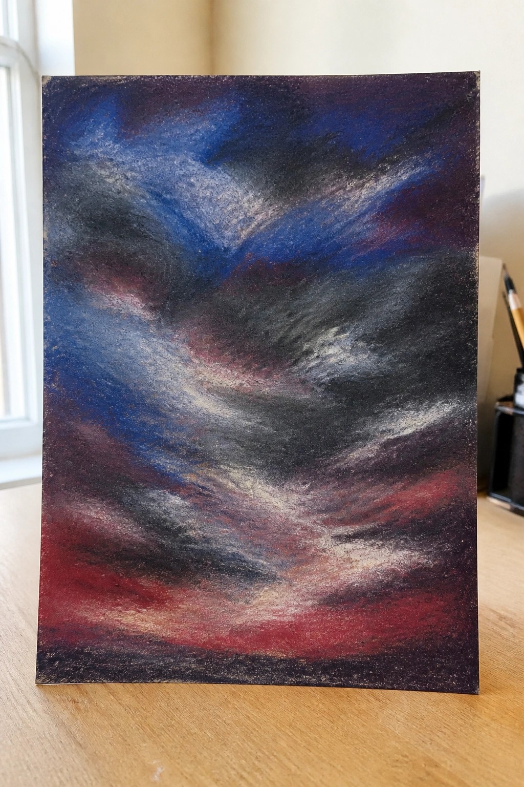 Abstract swirling sky painting in blues, purples, and reds on wooden table.